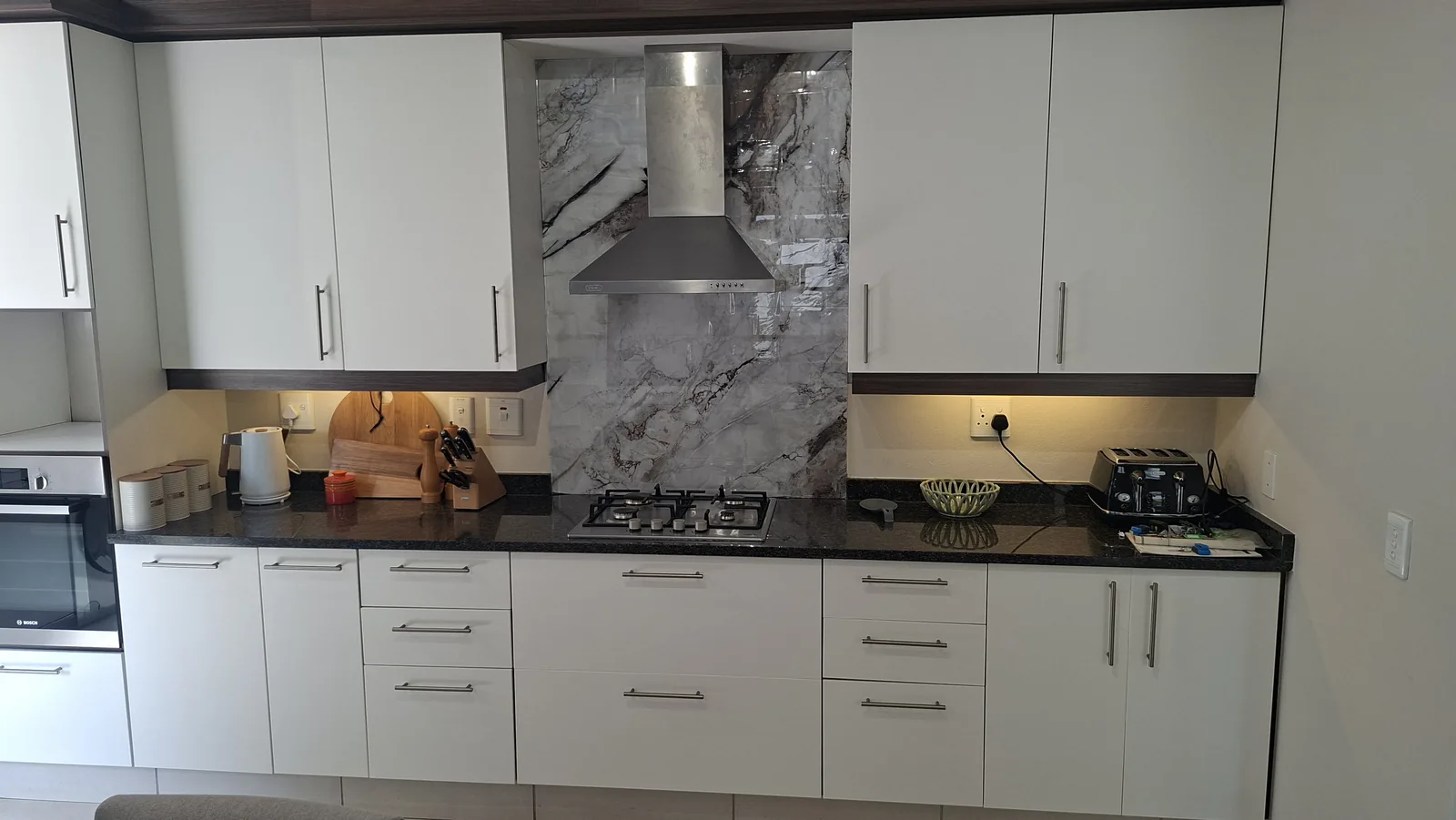 Wrapped kitchen cupboards and stone-look splashback around an extractor hood, Durban