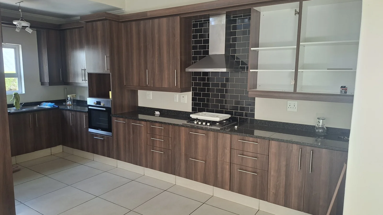Kitchen before wrapping, dark walnut cupboard doors and black subway tile splashback in a Durban home