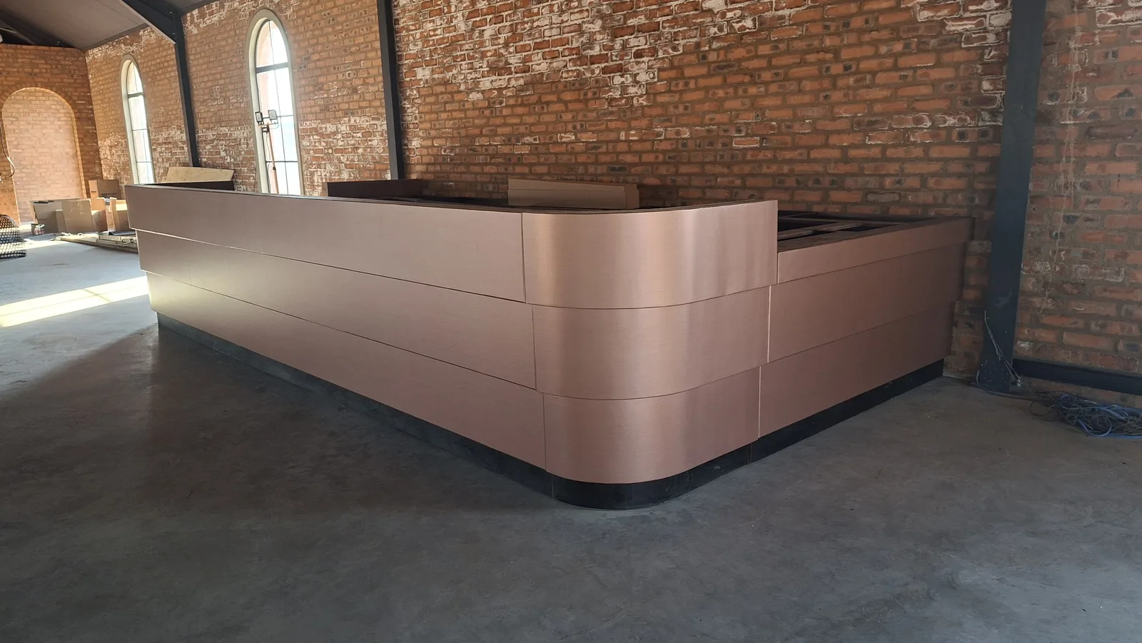 Curved reception counter wrapped in copper architectural film against an exposed brick wall